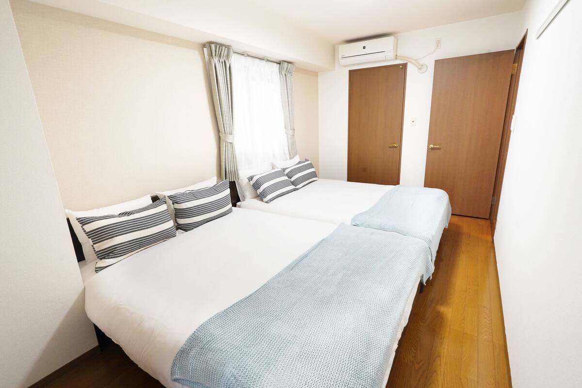 Ein Schlafzimmer mit zwei Betten, einem Fenster mit Vorhängen, einer Klimaanlage und Holzboden.