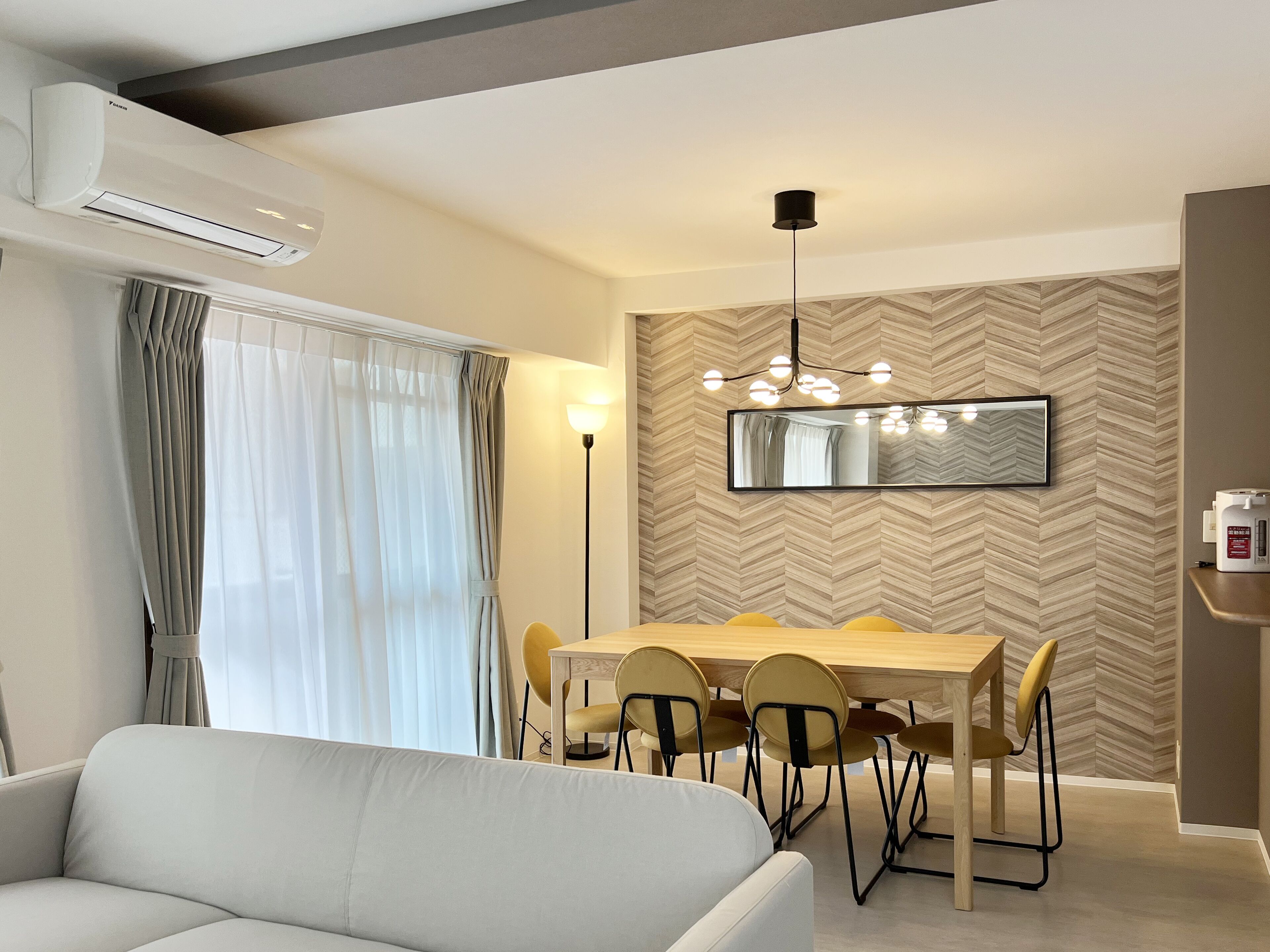 A modern dining area with a wooden table and chairs, a pendant light, and a large mirror on the wall.