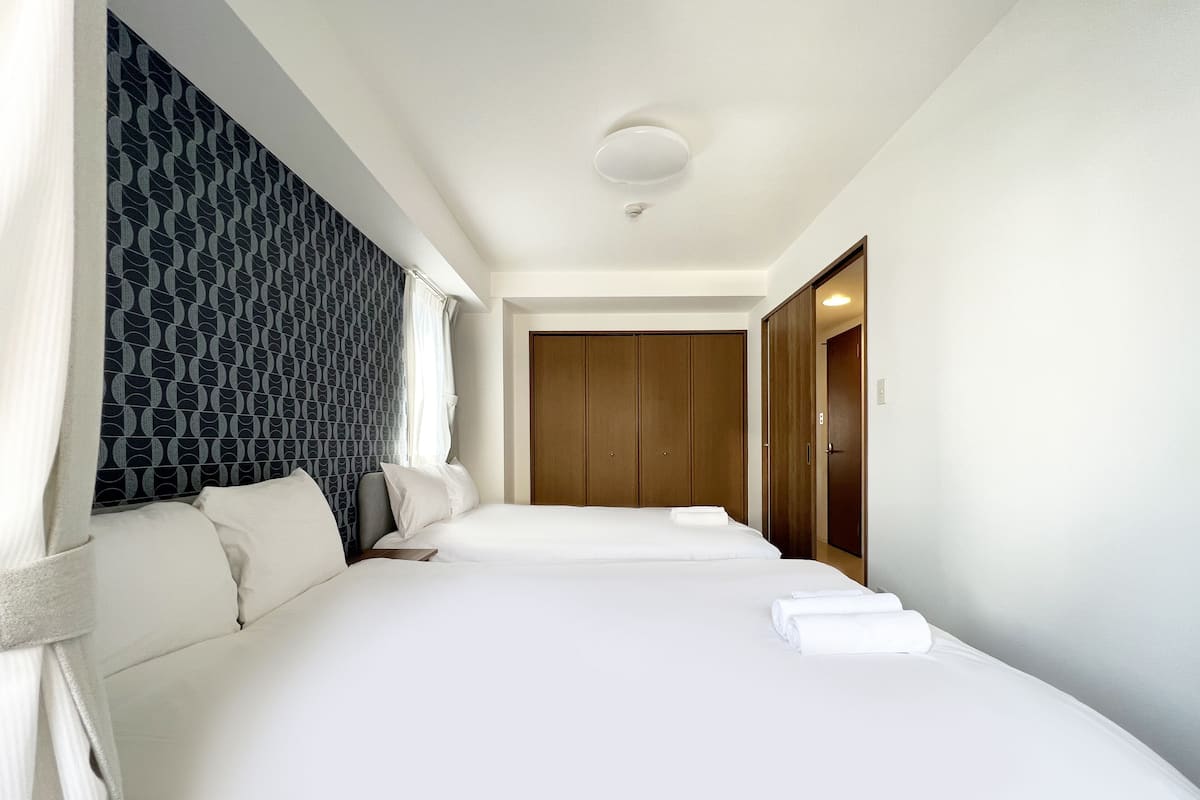 Ein Hotelzimmer mit zwei Betten, einem gemusterten Kopfteil, einem Holzschrank und einer weißen Decke.