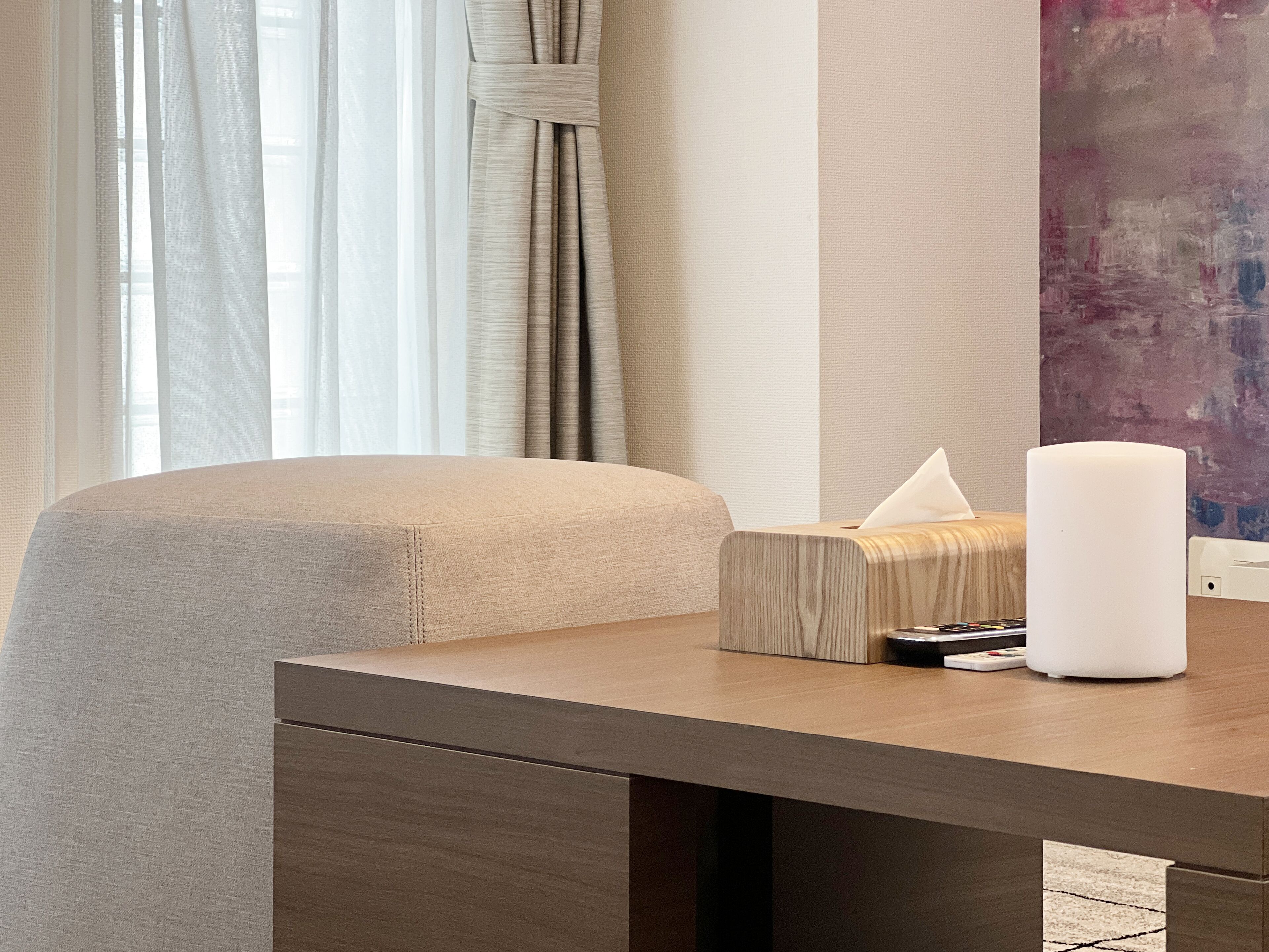 A modern hotel room with a wooden desk, a tissue box, a remote control, and a white candle.