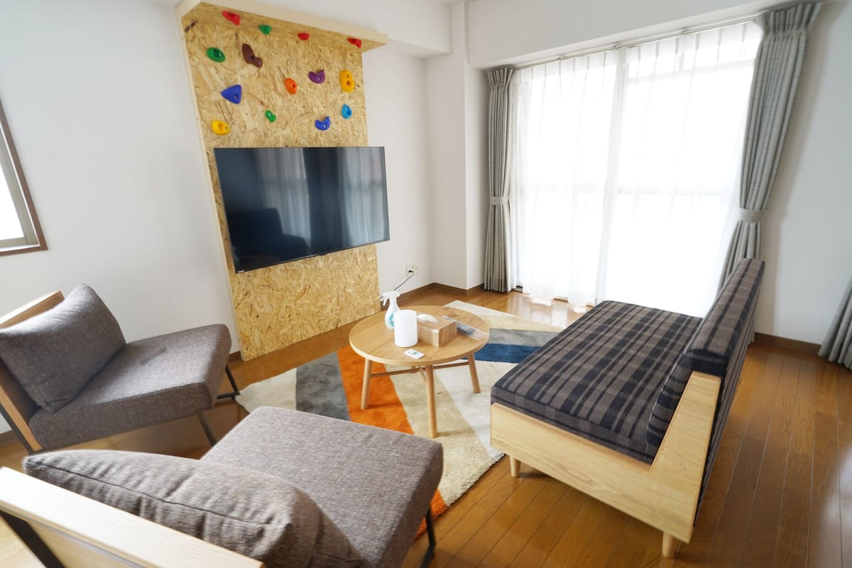 Ein modernes Zimmer mit Bett, Sofa, Fernseher und einer Kletterwand.