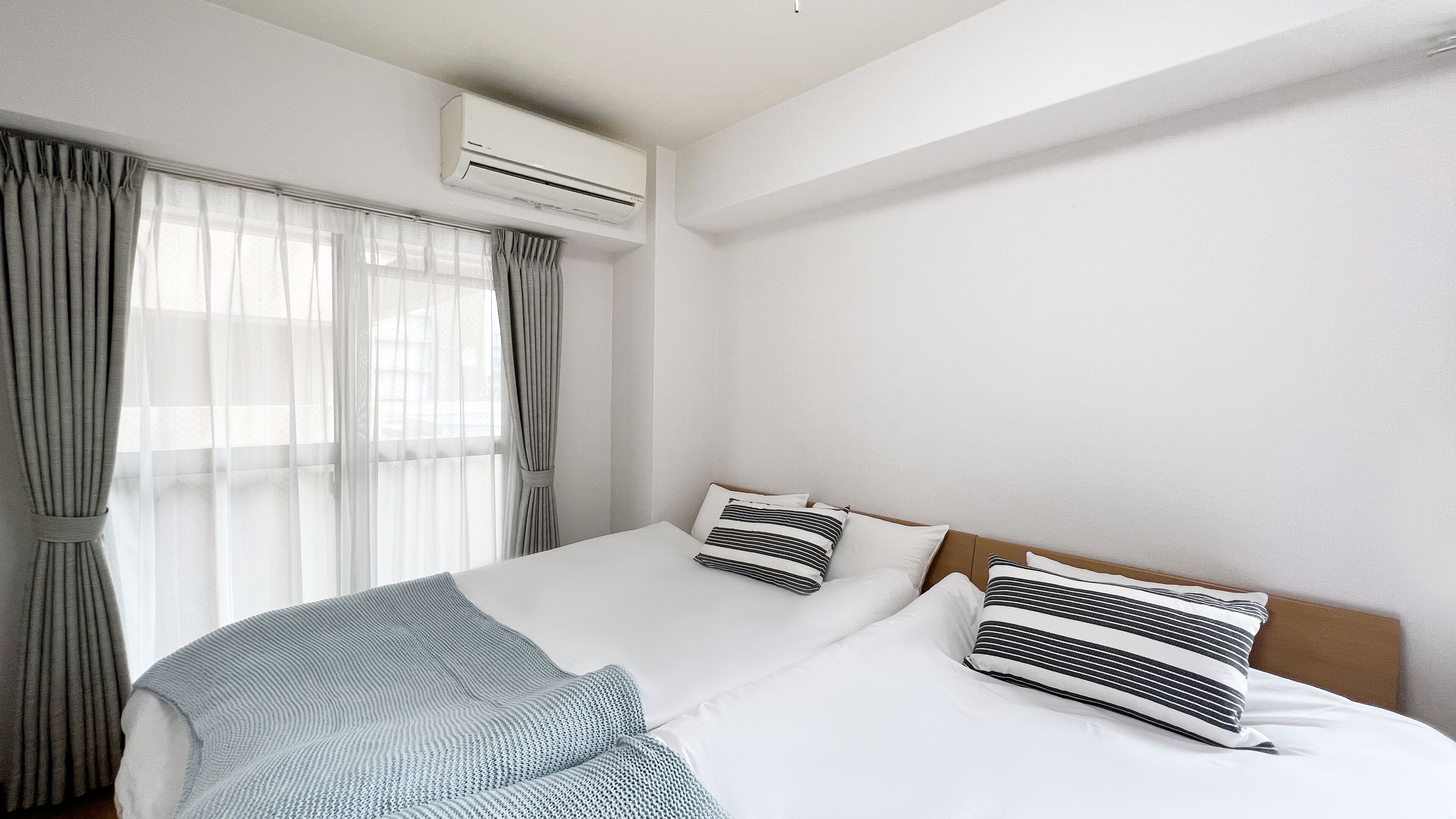 A hotel room with a bed, curtains, an air conditioning unit, and a window.
