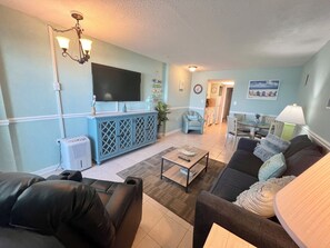 A living room with a TV, a blue cabinet, a sofa, and a dining area in the background. - Oceanfront 1BR condo with balcony views and direct beach access. (North Myrtle Beach)