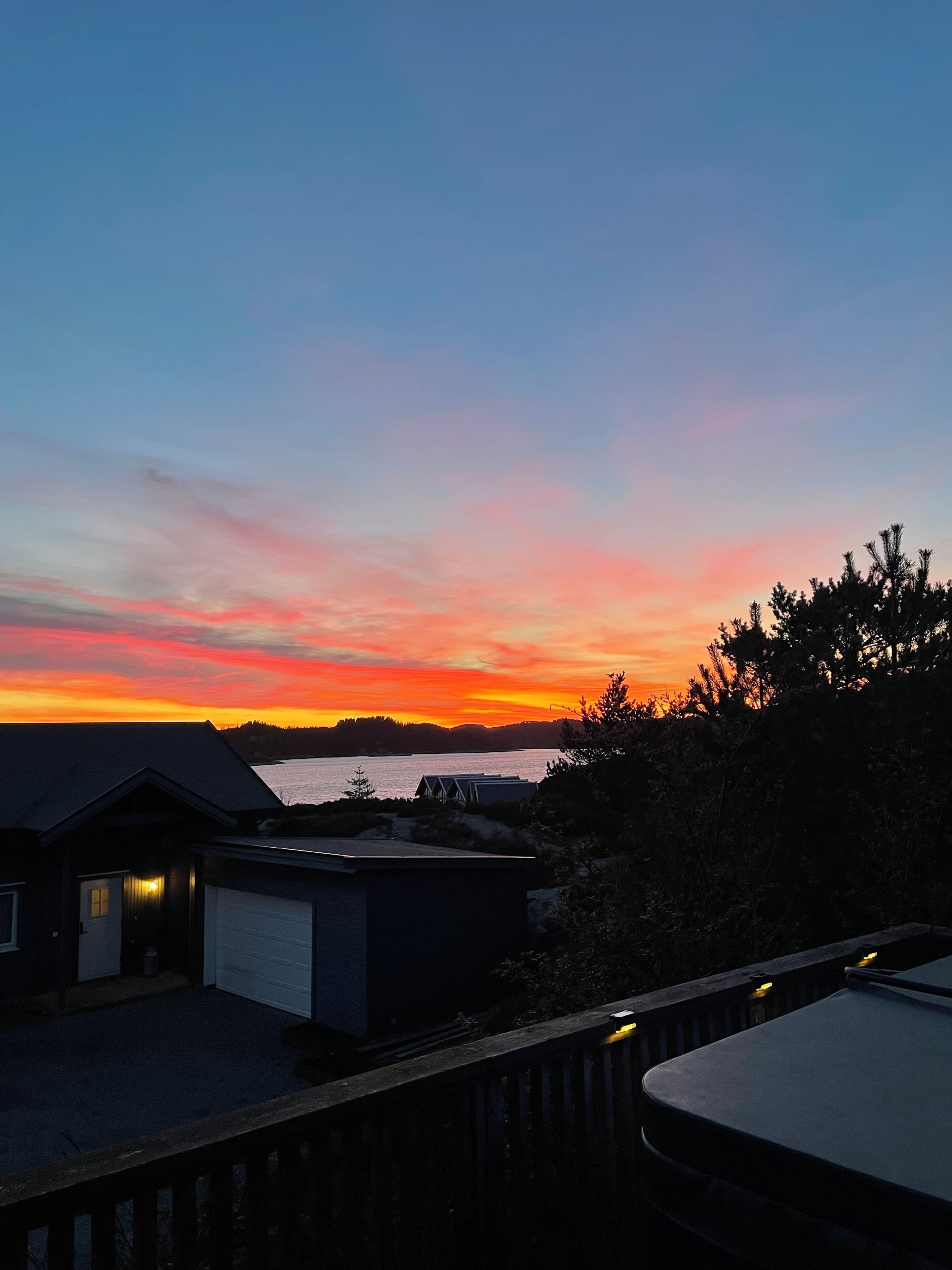 Vista do pôr do sol com um corpo d'água, um pequeno edifício e um deck de madeira.