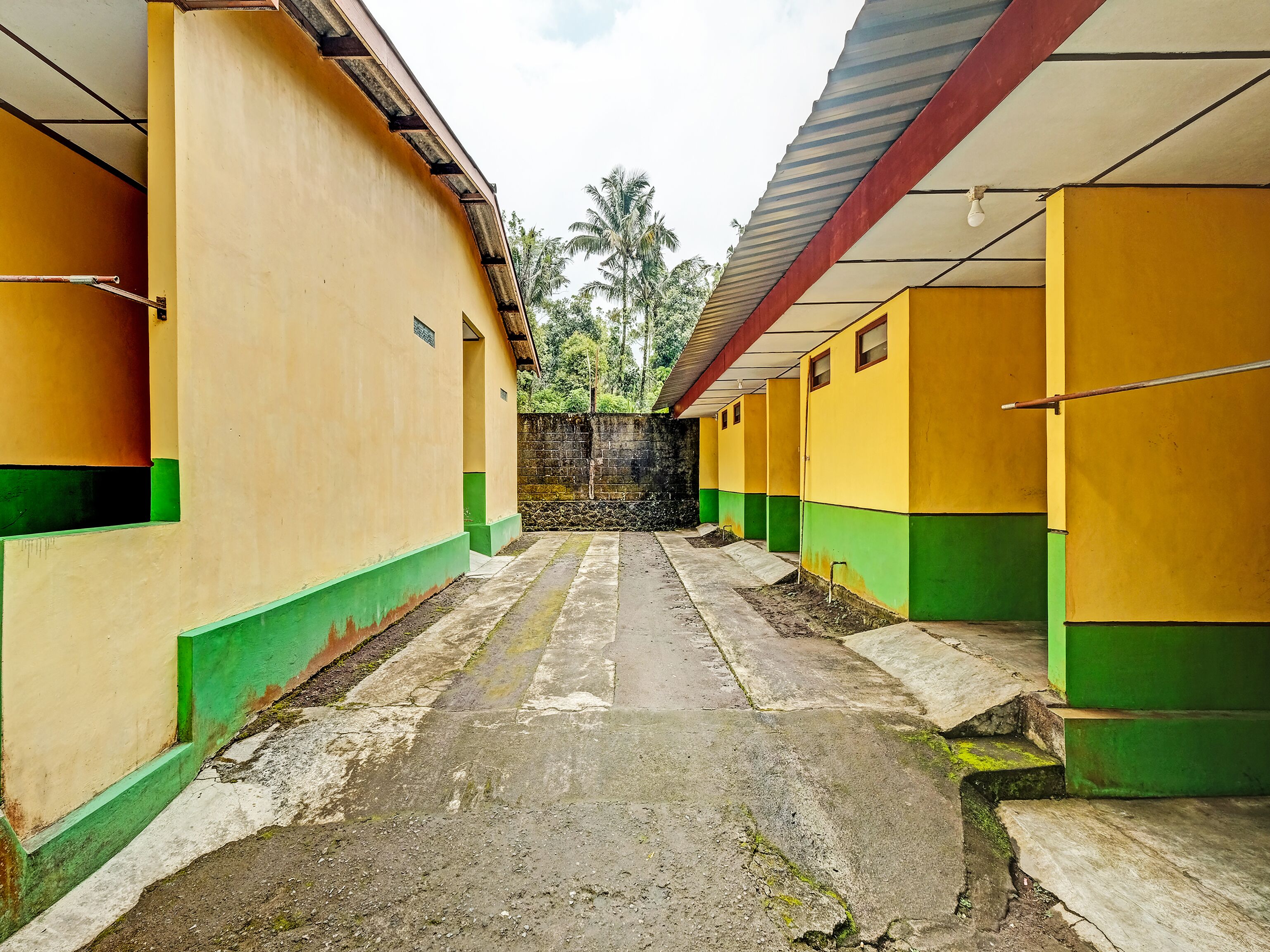Een rij gele en groene kamers met een betonnen vloer en een stenen muur op de achtergrond.