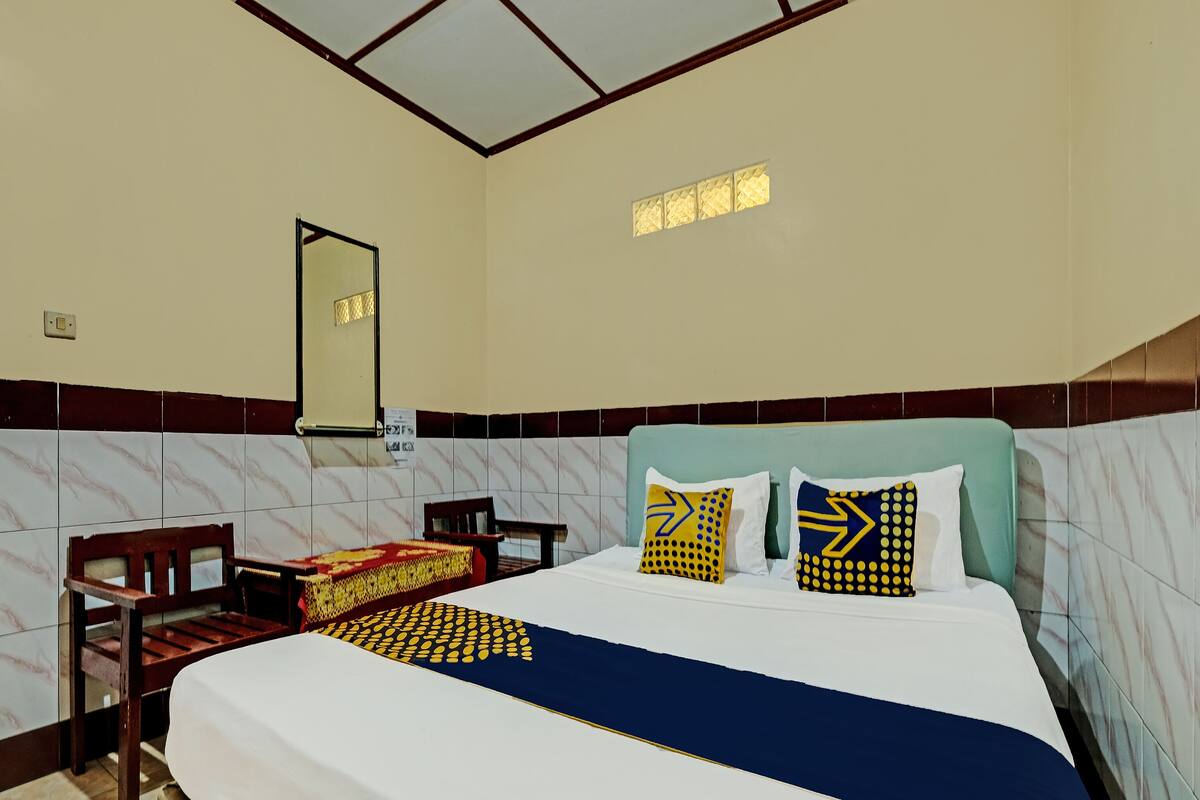 A neatly arranged hotel room with a bed, a chair, a desk, and a mirror.