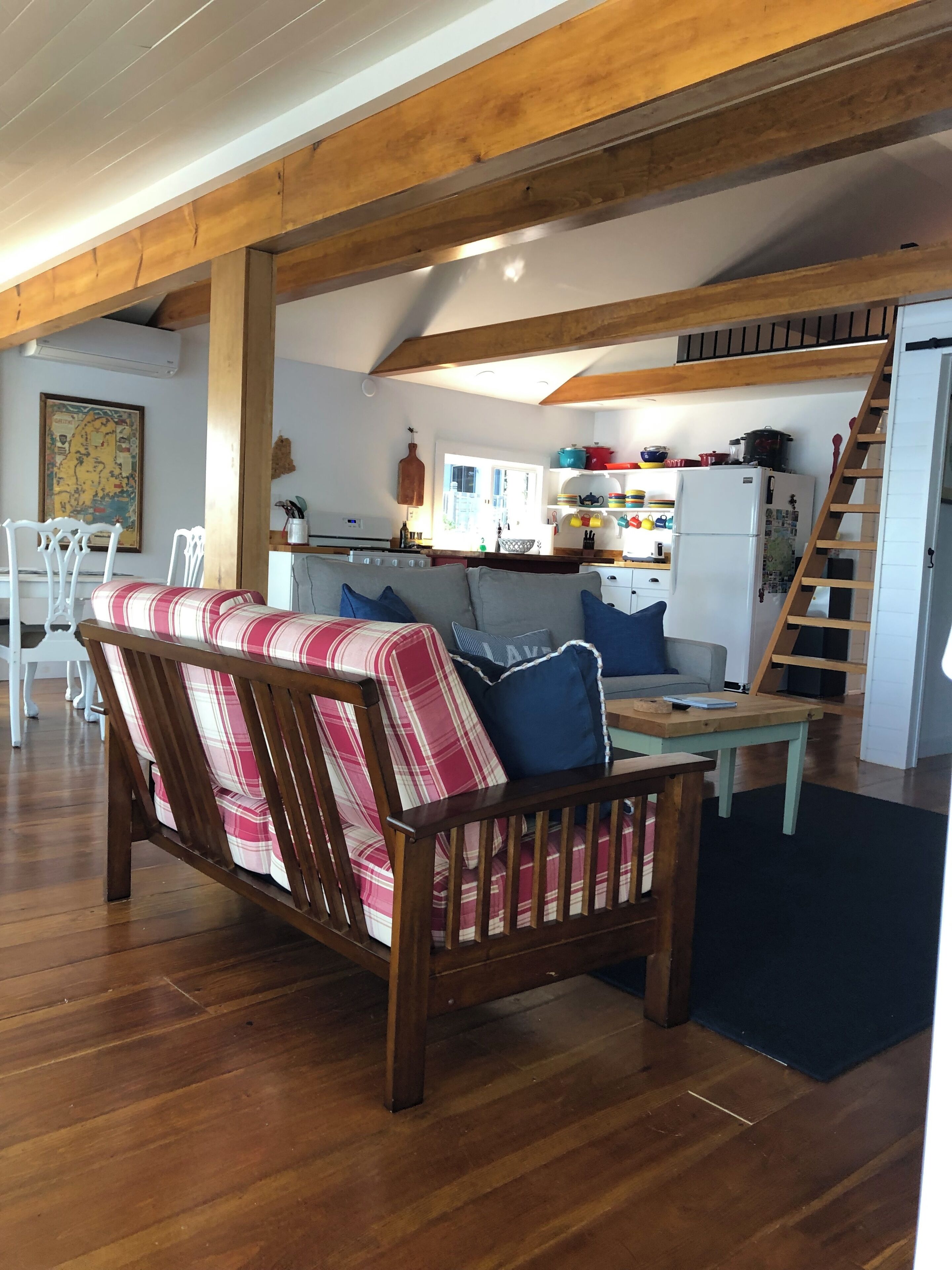 A cozy living area with a wooden sofa, a dining table, and a kitchen in the background.
