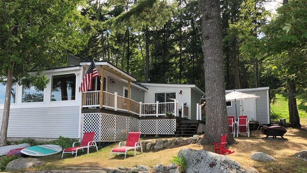 A cabin with a deck, outdoor seating, and a small dock. - Charming 3-bedroom house with WiFi, AC near Acadia National Park! (Otis)