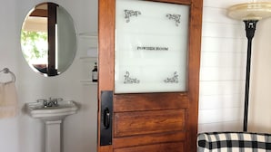 A powder room with a wooden door, a white sink, and a checkered chair. - Charming 3-bedroom house with WiFi, AC near Acadia National Park! (Otis)