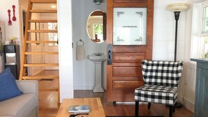 A cozy living room with a wooden table, a checkered chair, a sofa, a staircase, and a powder room sign. - Charming 3-bedroom house with WiFi, AC near Acadia National Park! (Otis)