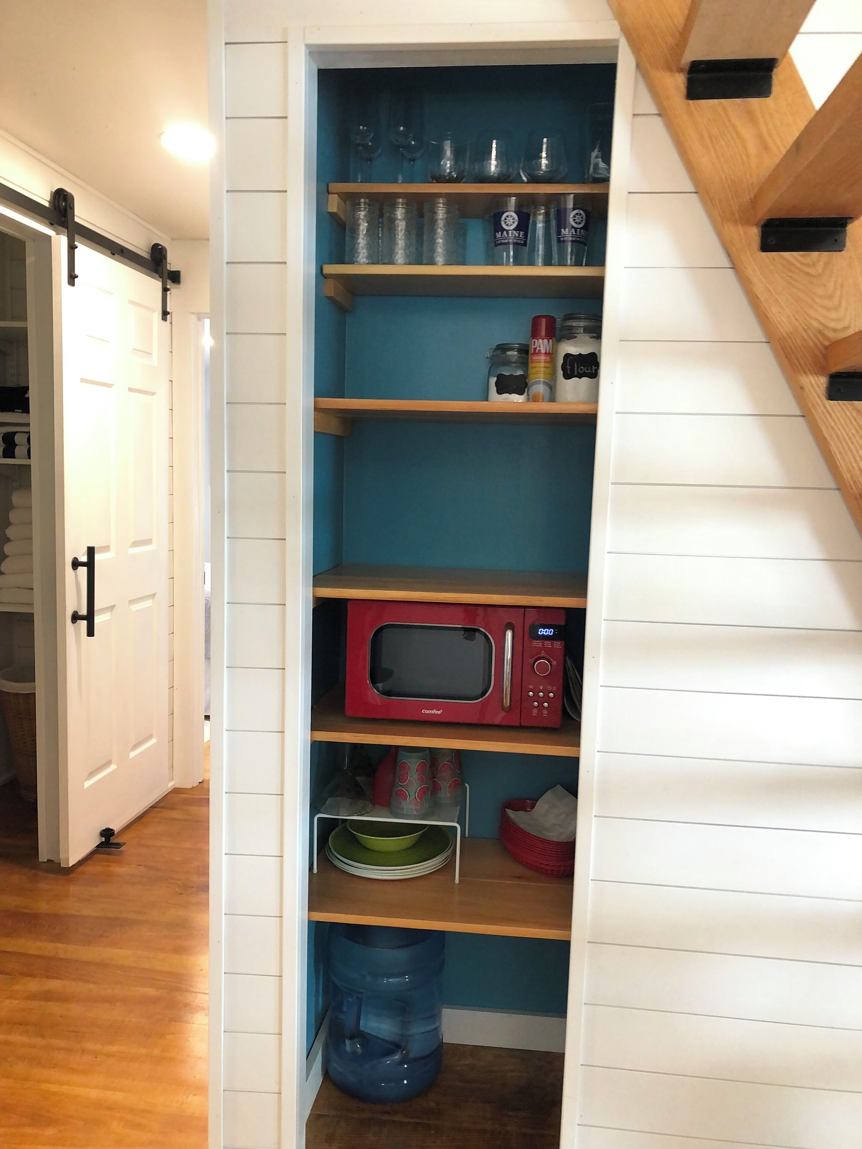 A kitchen with a red microwave, shelves with jars, and a water dispenser.