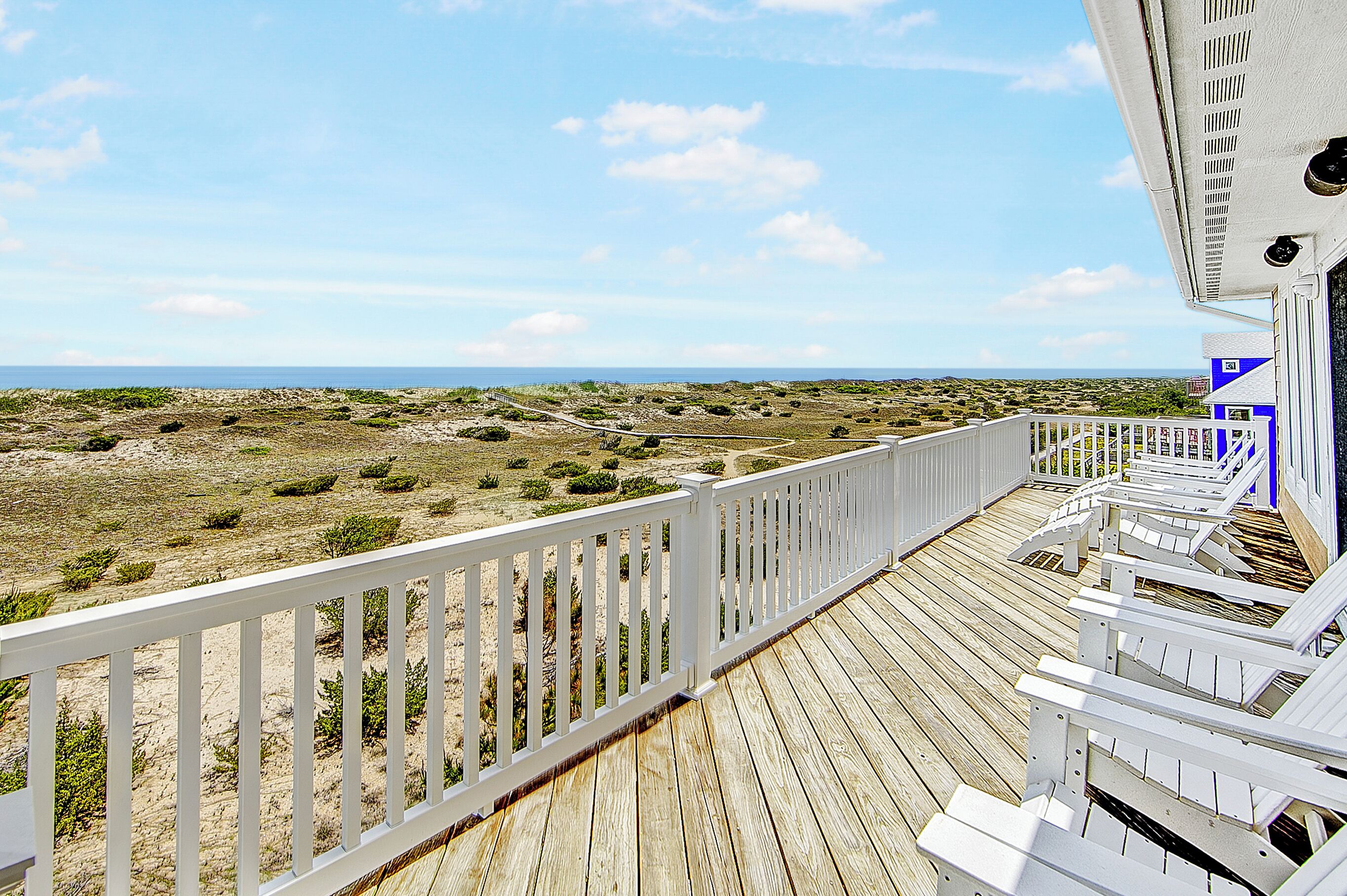 Une terrasse dotée de balustrades blanches, qui offre une vue sur une plage à la végétation clairsemée et un ciel dégagé.