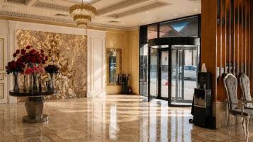 A hotel lobby with a marble floor, a round table with flowers, a chandelier, and a revolving door.