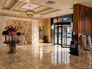 A hotel lobby with a marble floor, a round table with flowers, a chandelier, and a revolving door. - VELARA HOTEL (Tashkent)