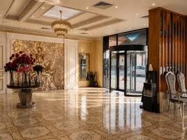 Vestíbulo de hotel con piso de mármol, una mesa redonda con flores, un candelabro y una puerta giratoria.