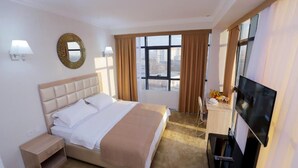 Ein Hotelzimmer mit einem großen Bett, einem Fernseher, einem Schreibtisch und einem Vorhangfenster.