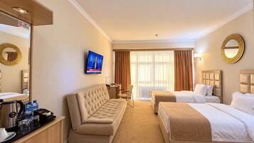A hotel room with a sofa, two beds, a TV, a desk, and a mirror.