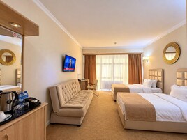 Habitación de hotel con sofá, dos camas, televisor, escritorio y espejo.
