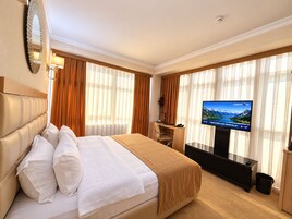 A hotel room with a bed, a desk, a television, and curtains.