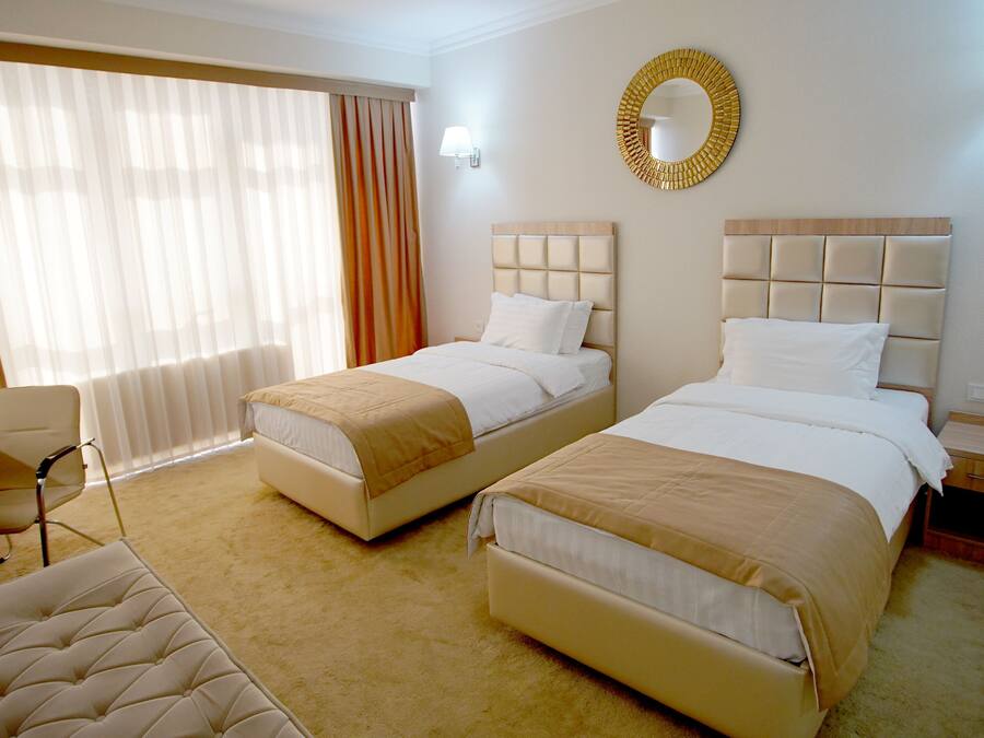 A hotel room with two beds, a desk, a chair, and a large window with curtains.