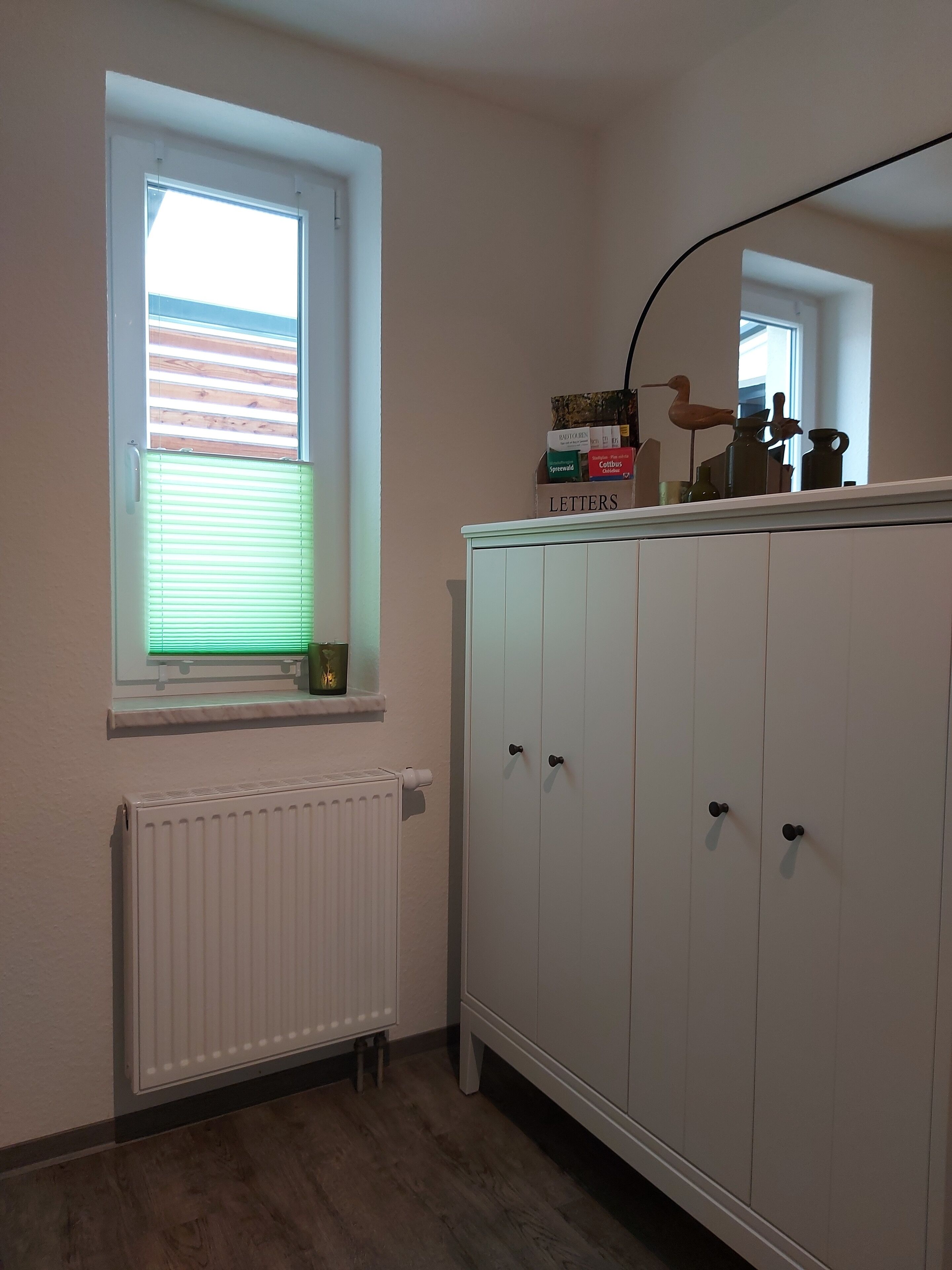 A room with a window, radiator, and a white wardrobe with multiple doors.