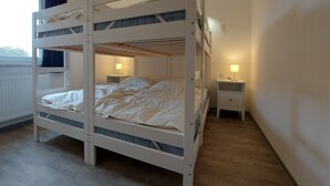 Een slaapkamer met een stapelbed, raam, nachtkastjes en een lamp.