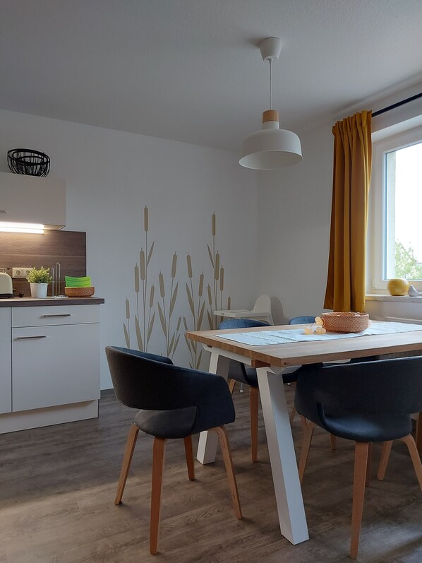 Une cuisine moderne avec des meubles blancs, un plan de travail en bois et un coin repas comprenant une table et des chaises.