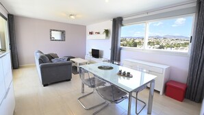 A modern living room with a sofa, a glass dining table, and a large window offering a city view. - A104 COSTA CALPE 3º-7 (Calpe)