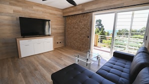 Una sala de estar moderna con un televisor de pantalla plana, una mesa de centro de vidrio y un sofá oscuro.