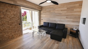 Una sala de estar moderna con un sofá seccional negro, una mesa de centro de vidrio y un ventilador de techo.