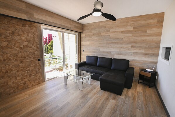 Una sala de estar moderna con un sofá seccional negro, una mesa de centro de vidrio y un ventilador de techo.