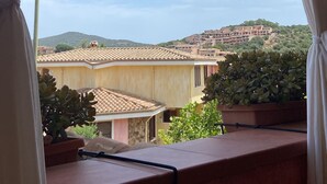 A balcony with a view of a hillside town, featuring terracotta-roofed buildings and greenery. - Comfortable and cozy Villasimius apartment 5 minutes from the center  (villasimius)