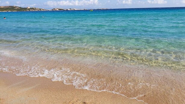 A beach with clear turquoise water, gentle waves, and distant rocky formations. - Comfortable and cozy Villasimius apartment 5 minutes from the center  (villasimius)