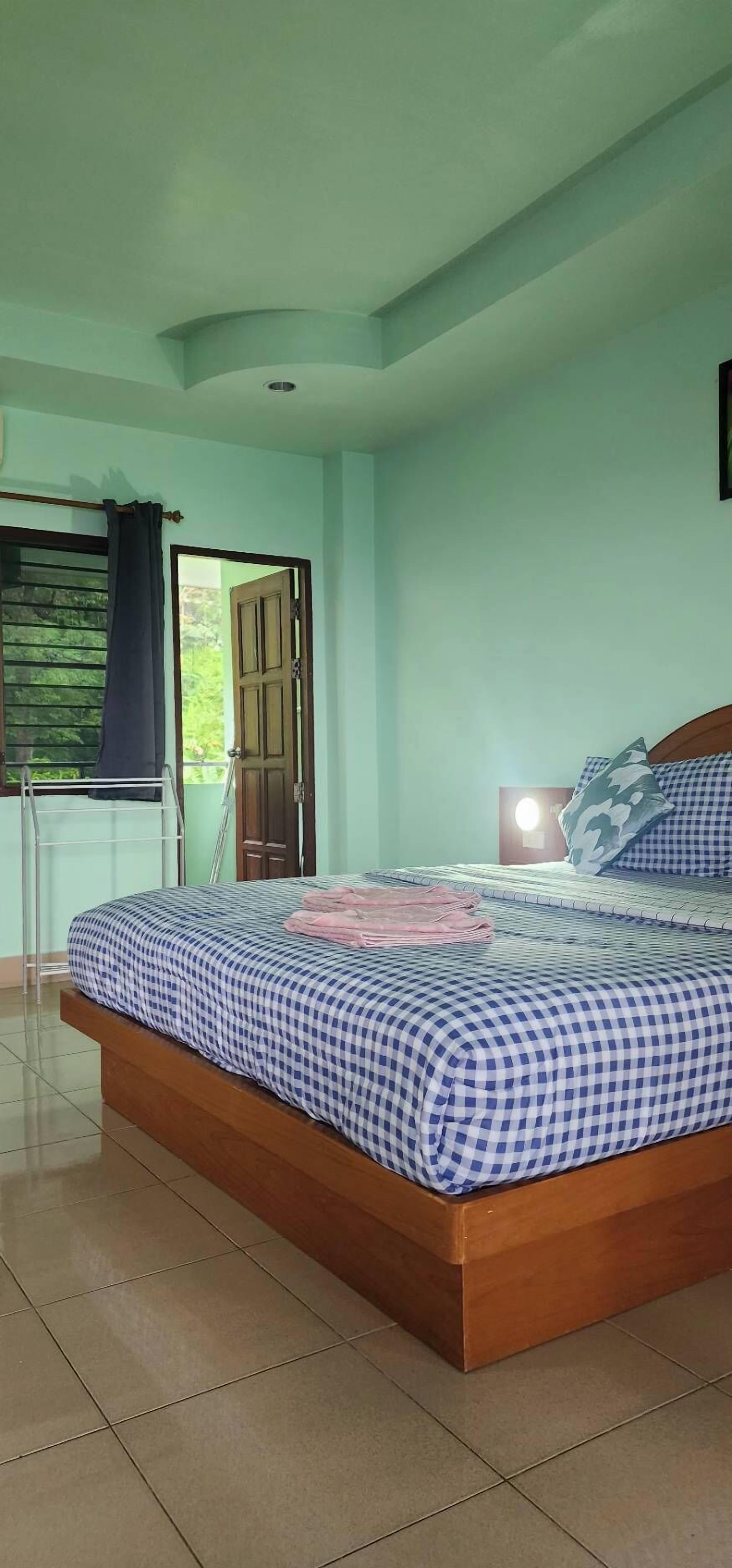 A bedroom with a bed, a nightstand, a window with curtains, and a view of greenery outside.