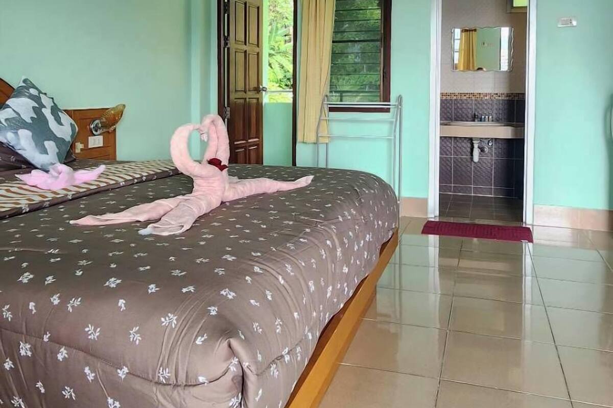 A bedroom with a bed, a window with curtains, an air conditioning unit, and a bathroom visible through an open door.