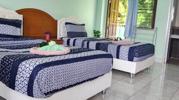 Une chambre d’hôtel avec un grand lit, un lit plus petit et un canapé-lit. Il y a une fenêtre donnant sur un paysage verdoyant.