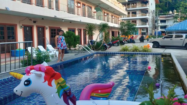 A swimming pool with a unicorn float, surrounded by a building with balconies and a few parked vehicles. - PAILIN HILL (Patong)