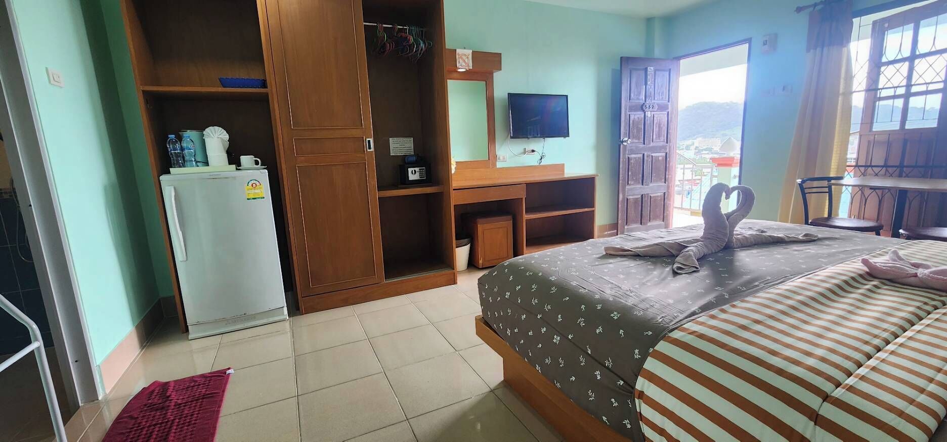 Un dormitorio con cama, armario, escritorio, televisor y balcón con vistas.