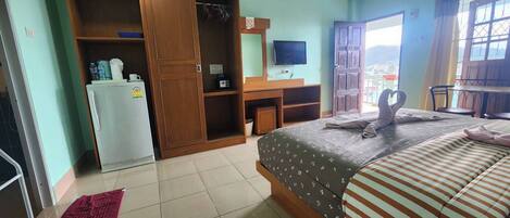 Un dormitorio con cama, armario, escritorio, televisor y balcón con vistas.