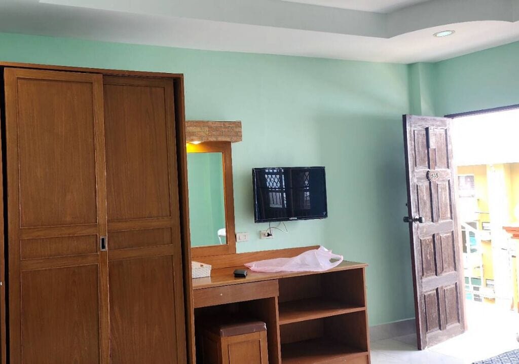 Una habitación con un armario de madera, un televisor montado en la pared y un escritorio de madera con un espejo.