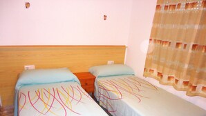 A room with two single beds, a wooden headboard, a small wooden nightstand, and a window with a sheer curtain. - El Peñon (Peñiscola)