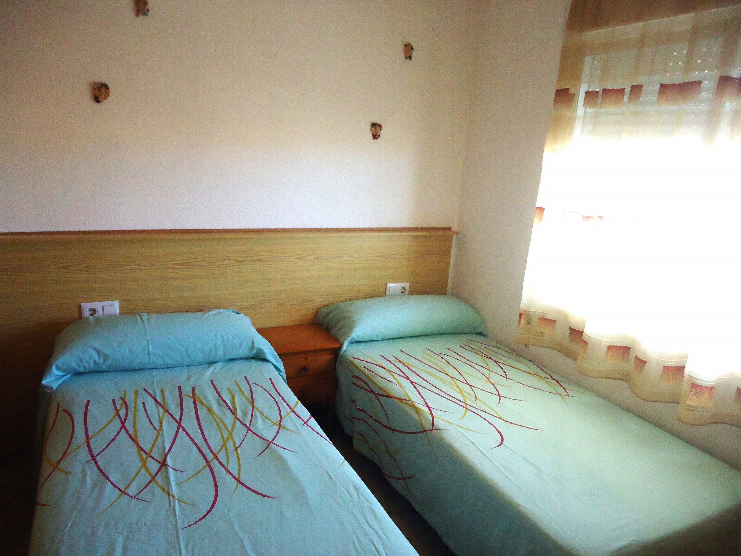 Una habitación con dos camas individuales, cabeceros de madera y una ventana con cortinas.