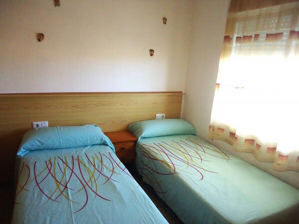 Une chambre avec deux lits simples, des têtes de lit en bois et une fenêtre avec des rideaux.