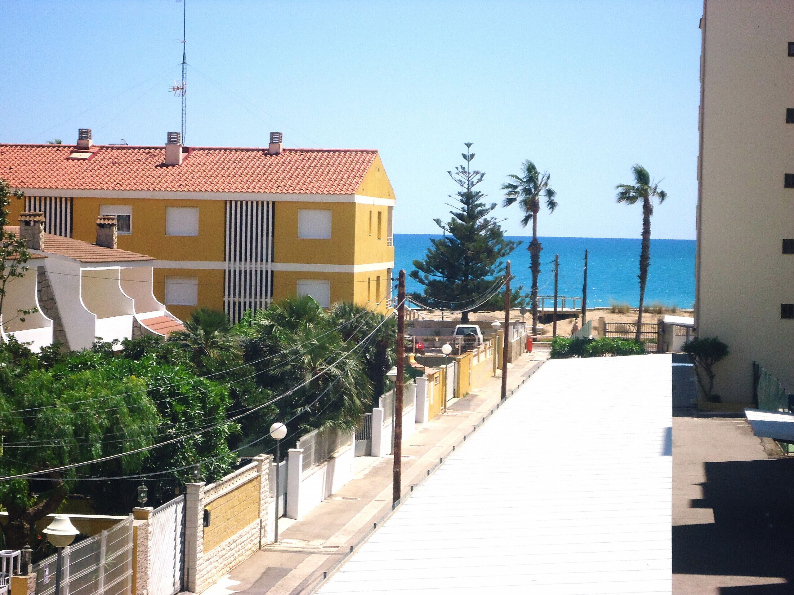 Una calle costera con edificios, cielo despejado y el mar al fondo.