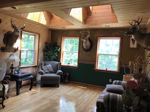 Une pièce chaleureuse avec un plancher en bois, un fauteuil confortable, une table avec une lampe et des bois de cerf accrochés aux murs.
