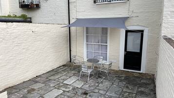 A small patio with a table and chairs, a grey umbrella, and a white brick wall.