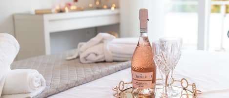 A bed with a rolled white towel, a bottle of Brilla! Prosecco Rosé, and two glasses on a tray.