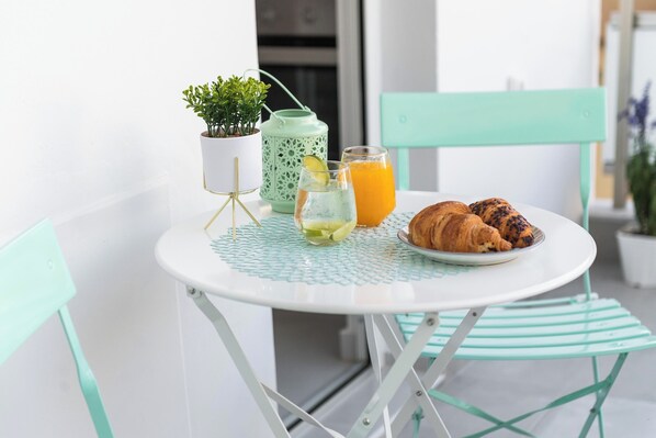 A round table with a white surface, a small potted plant, a glass of orange juice, a glass of water with a lemon slice, and a plate with croissants. - Sweet Dream Premium Apartment (Rhodes)