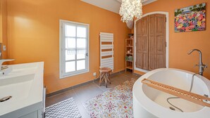 Un baño con una bañera, un lavamanos blanco, una puerta de madera y una alfombra colorida.