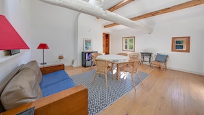 Amplia sala de estar con techo alto, vigas de madera, una mesa de comedor con sillas, un sofá y una lámpara roja.